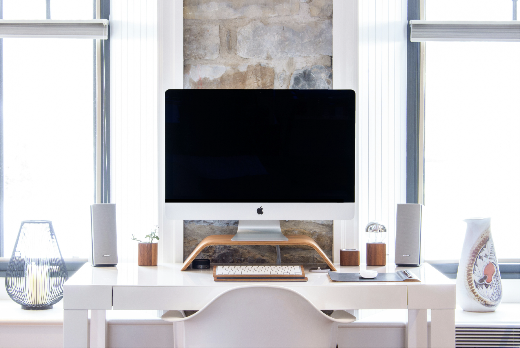 computer sitting on white desk in between two windows